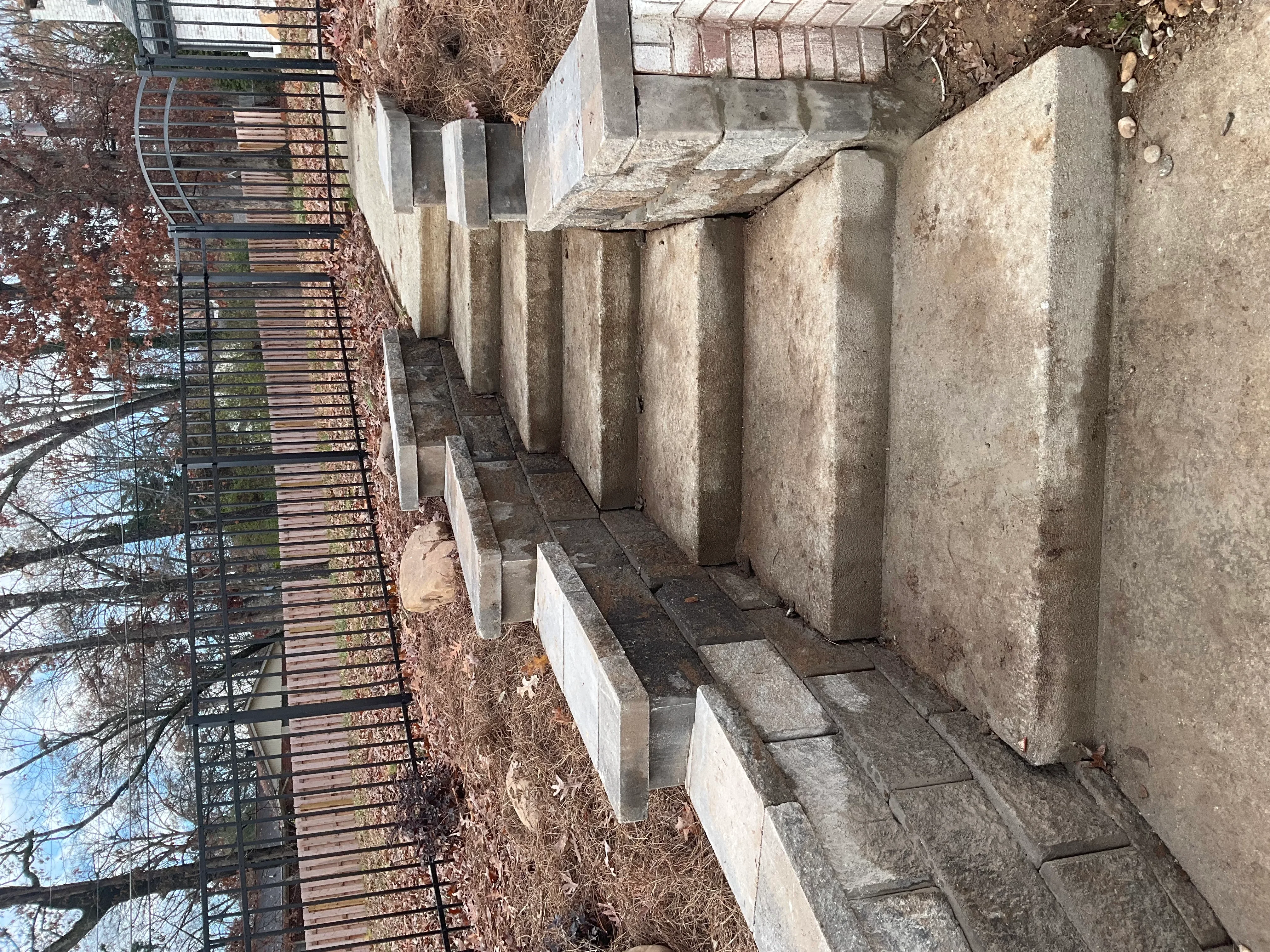Multi-tiered concrete retaining wall with stacked blocks and metal railing along residential property