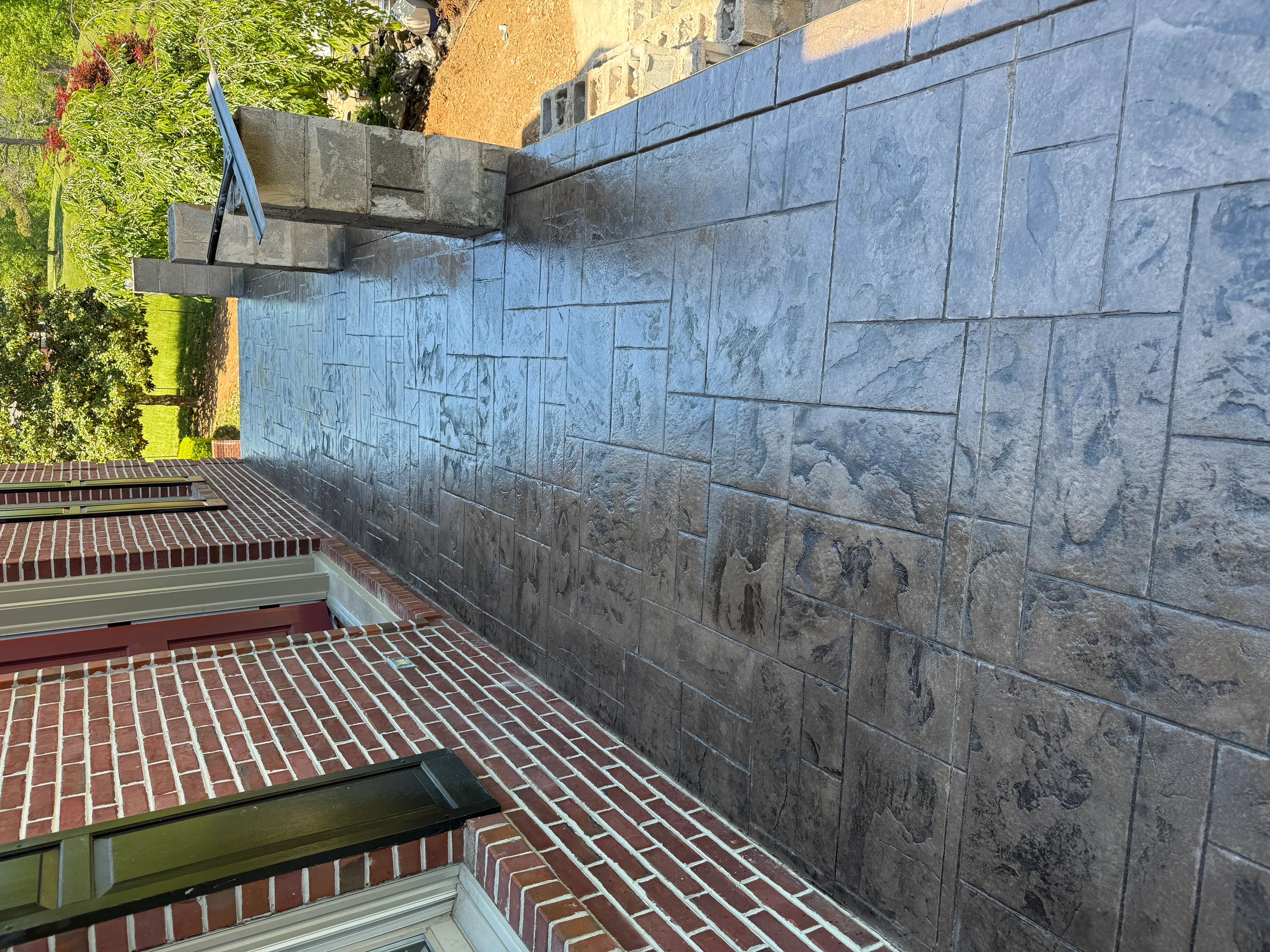 Gray concrete block retaining wall with red brick patio and green landscaping