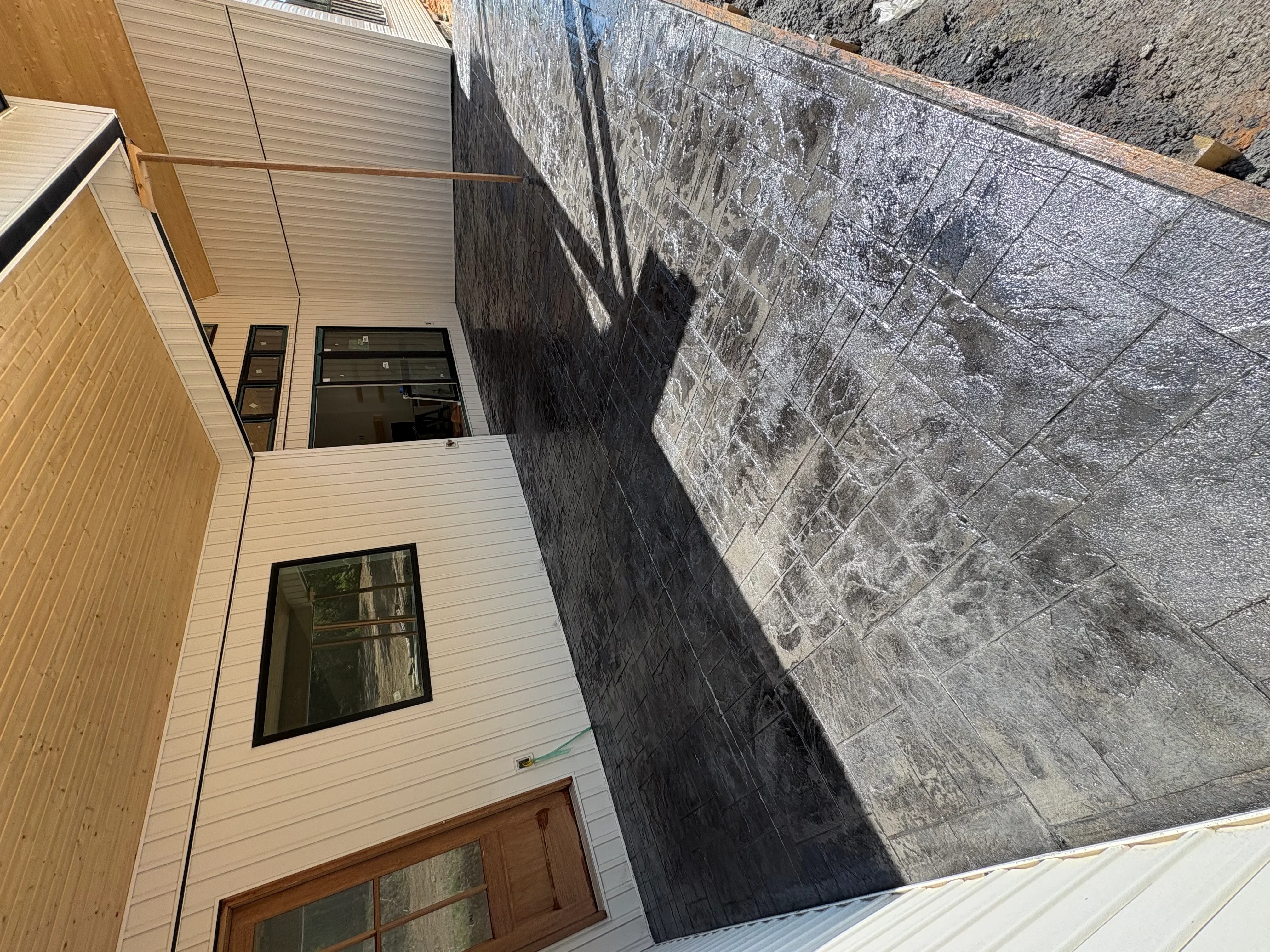 Gray concrete block retaining wall alongside new cream-colored residential siding