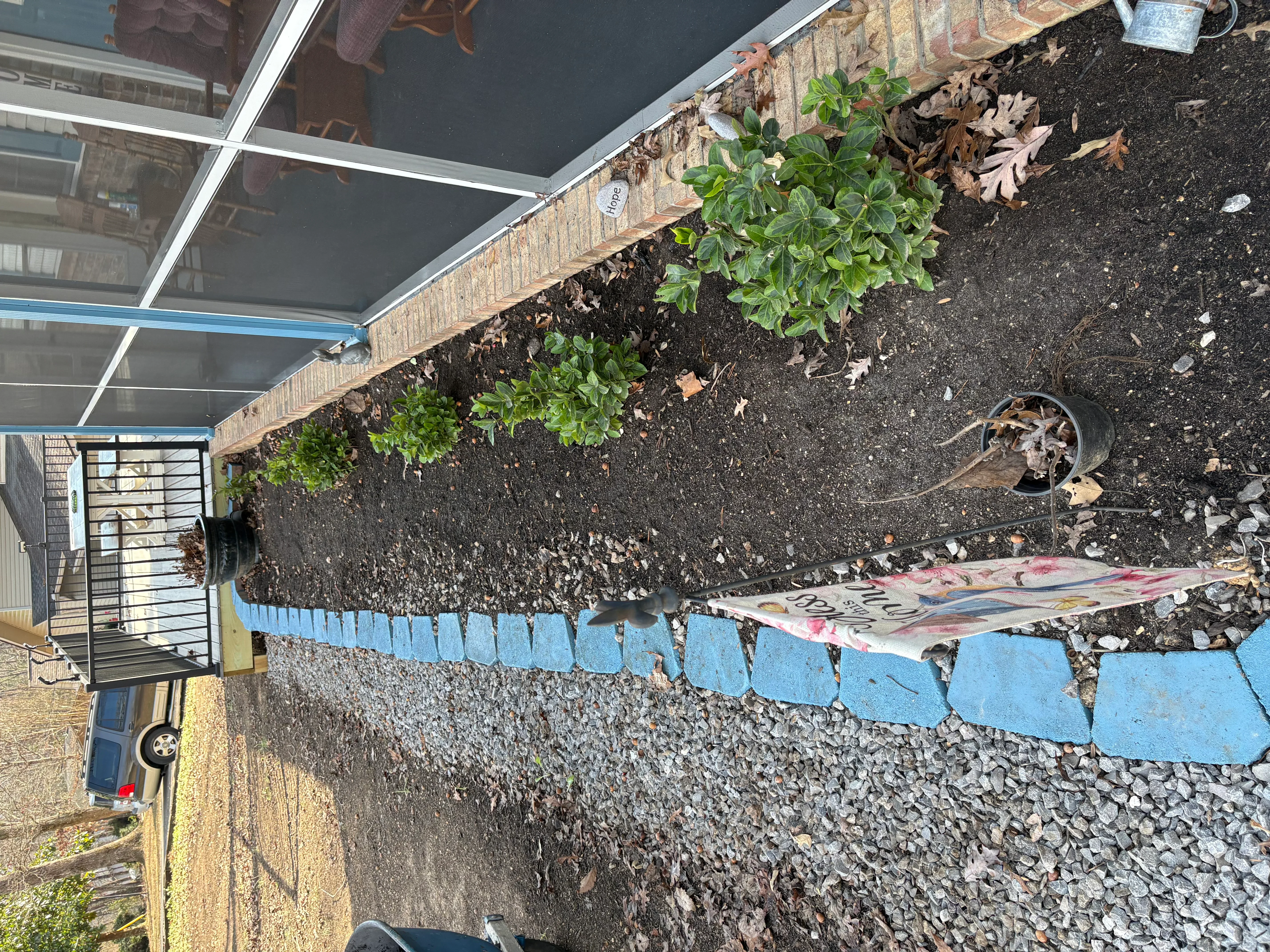 Raised garden bed with blue concrete edging, dark soil, and green plants under clear roof panels