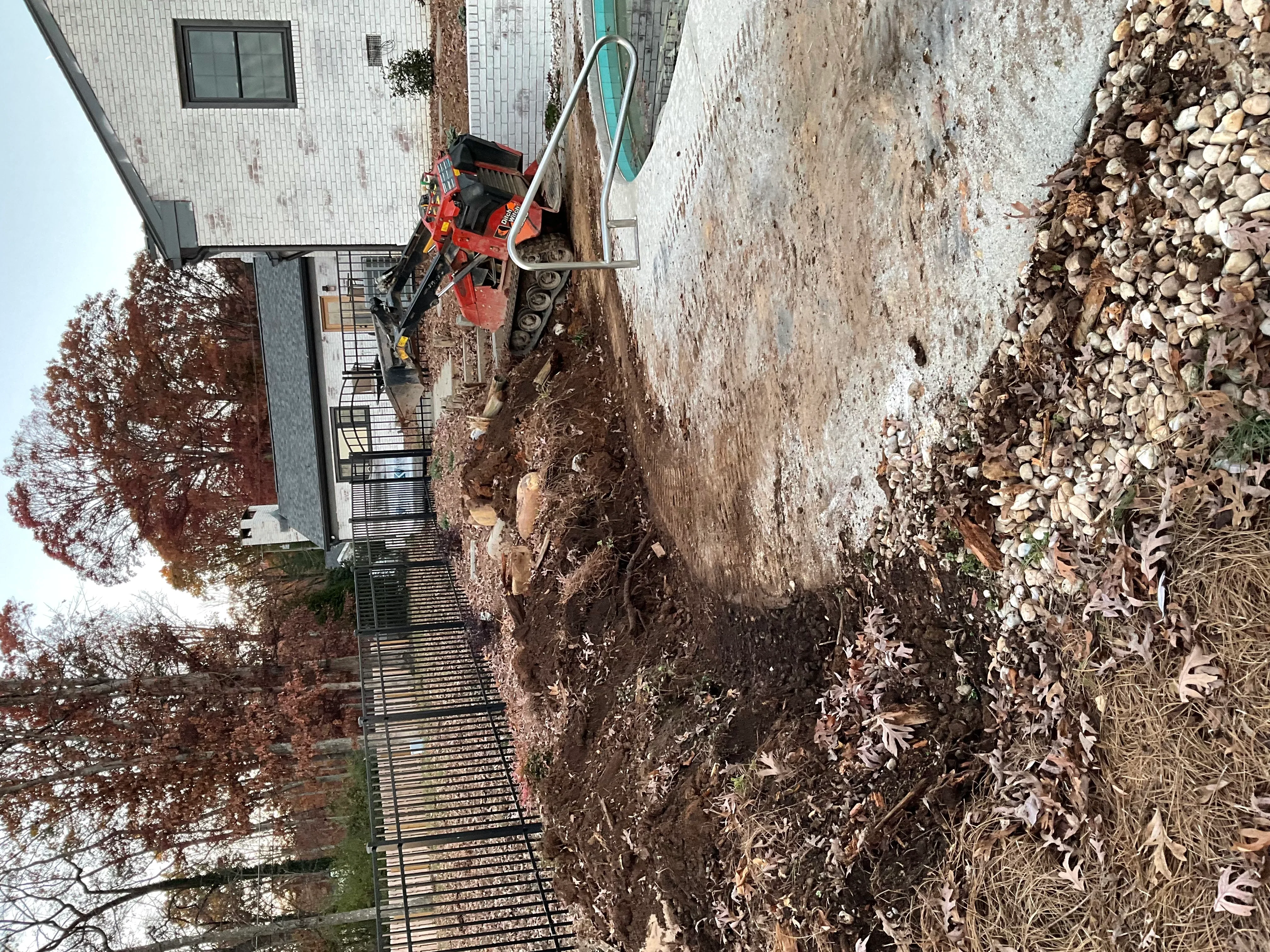 Red excavator on residential driveway site with crushed stone base and metal drainage grates