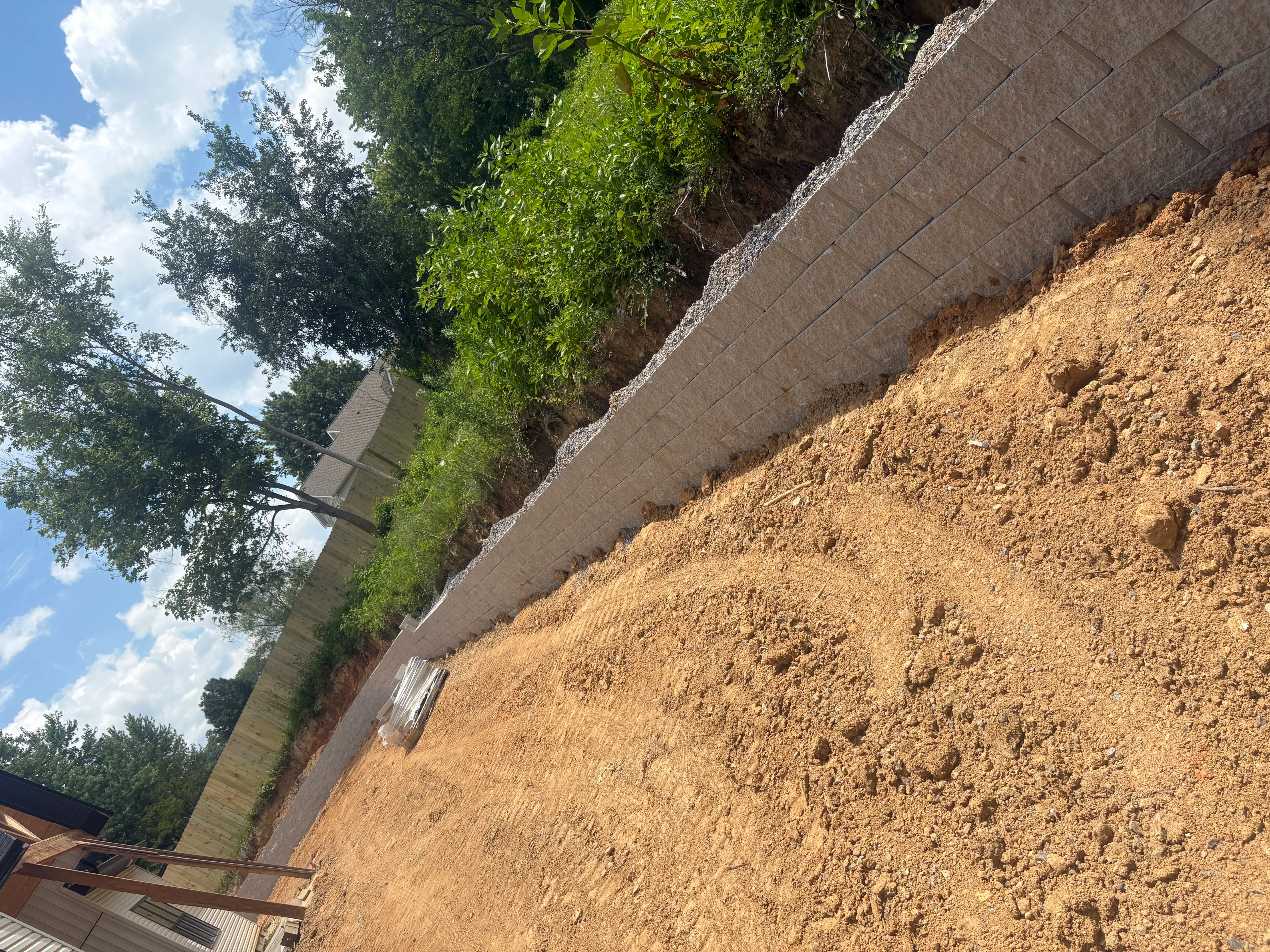 Concrete retaining wall with herringbone block pattern and gravel drainage base on sloped terrain