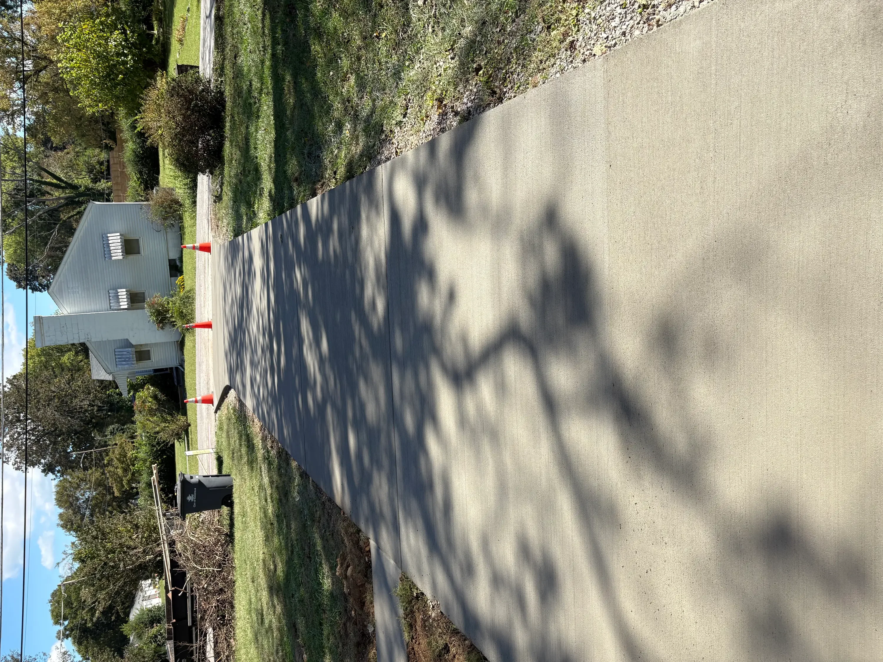 Newly poured concrete driveway with red markers and mature landscaping