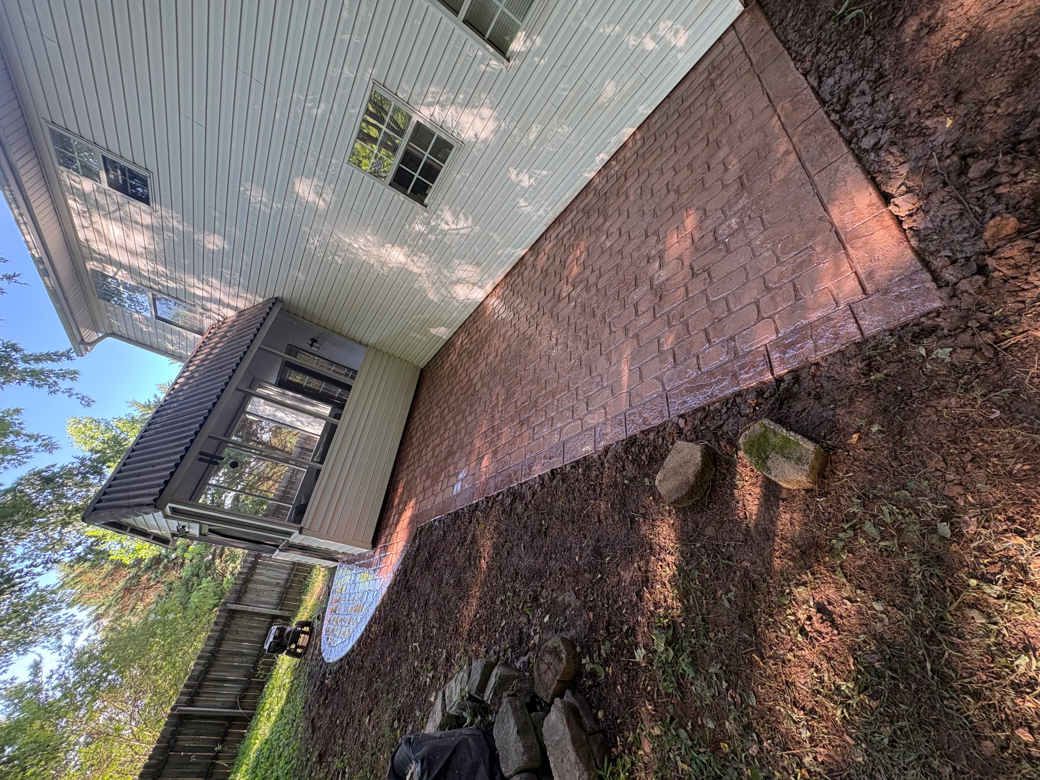 Cleaned brick foundation wall next to metal-sided building with visible restoration results