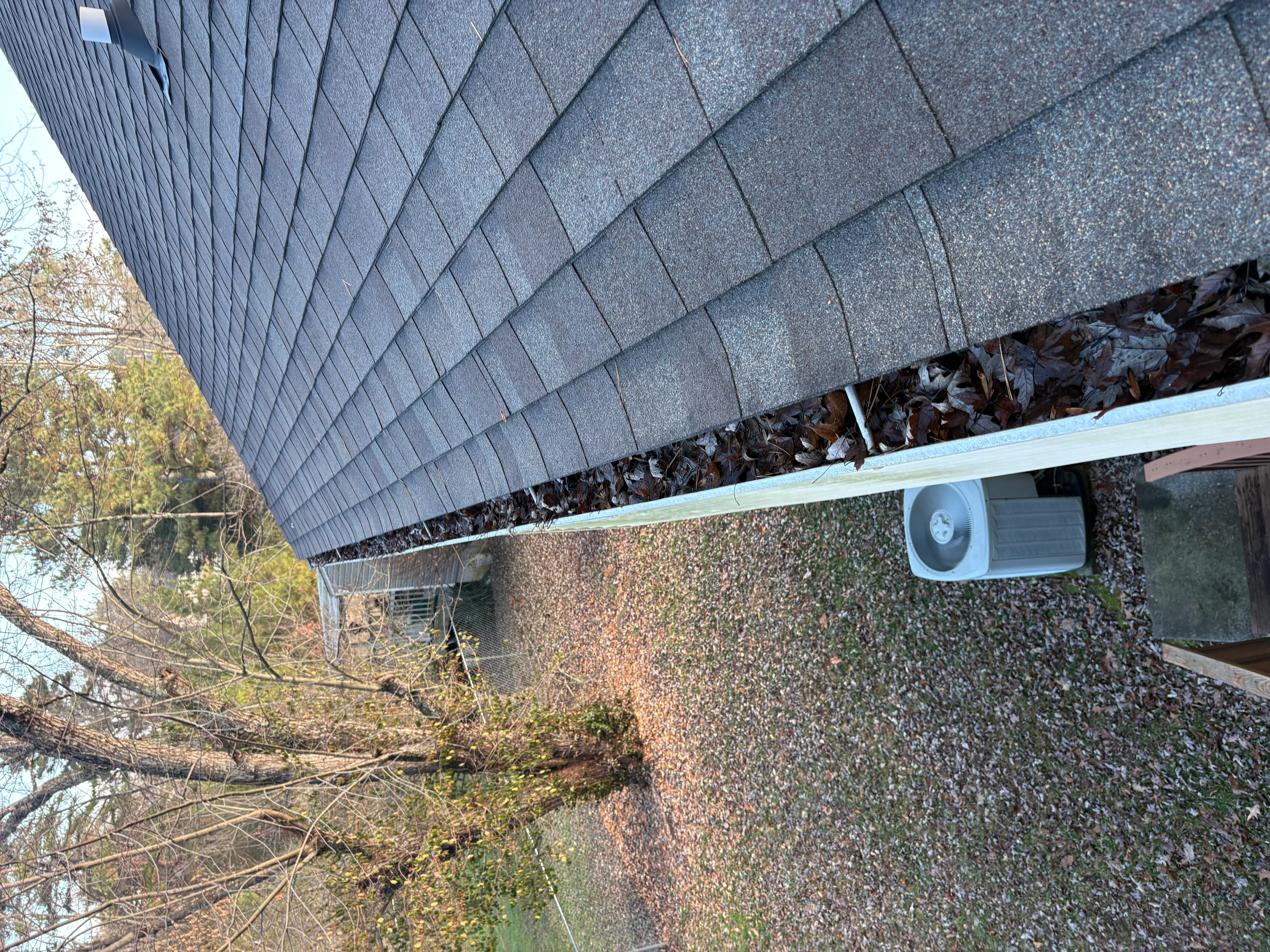 Residential roof with dark shingles and cleaned gutters, showing gutter line and downspout