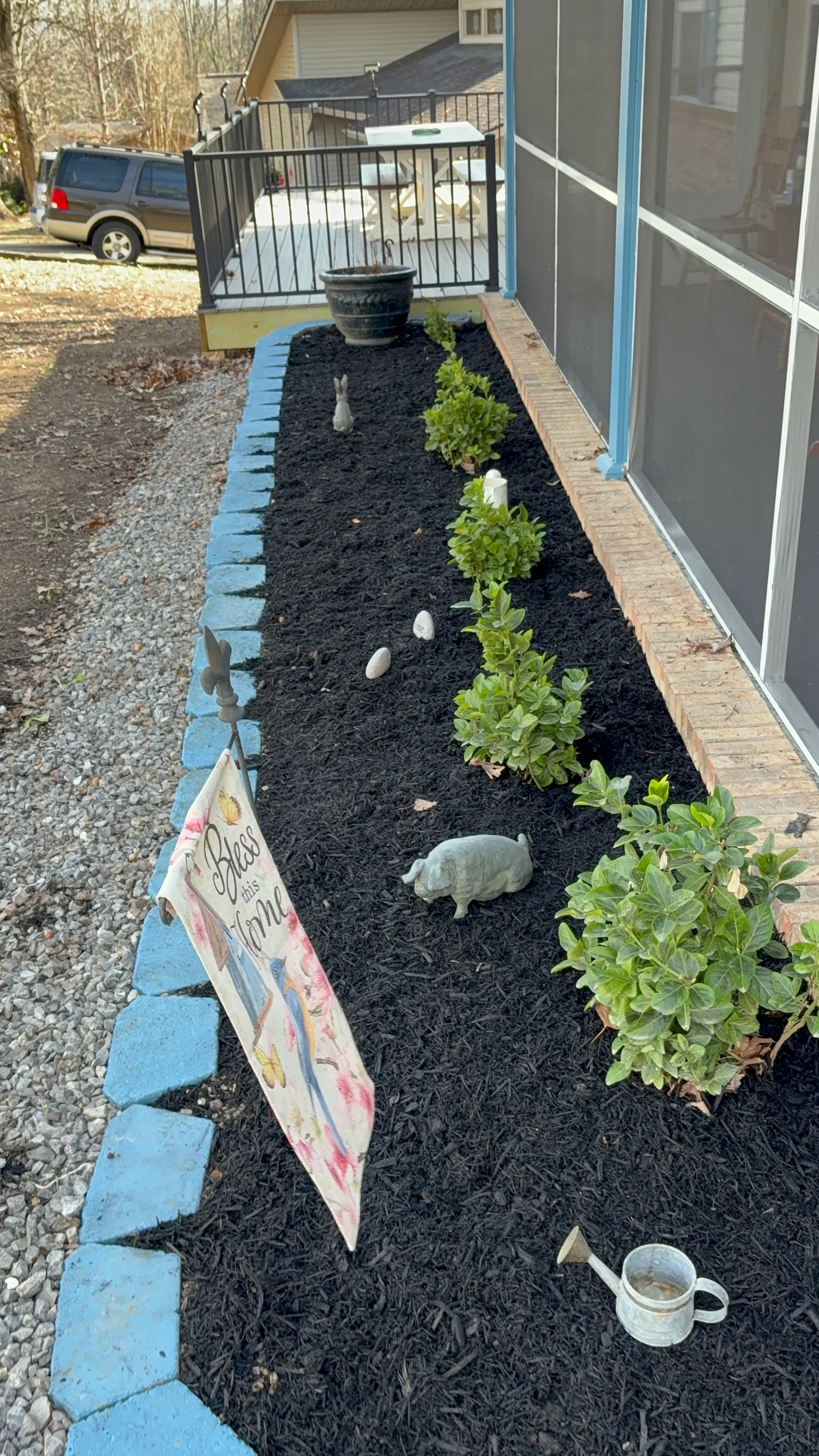 Blue concrete edging borders a foundation planting bed with black mulch and green shrubs