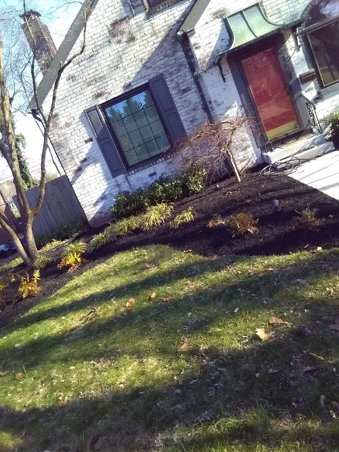 Brick home foundation with fresh dark mulch bed and newly planted ornamental grasses