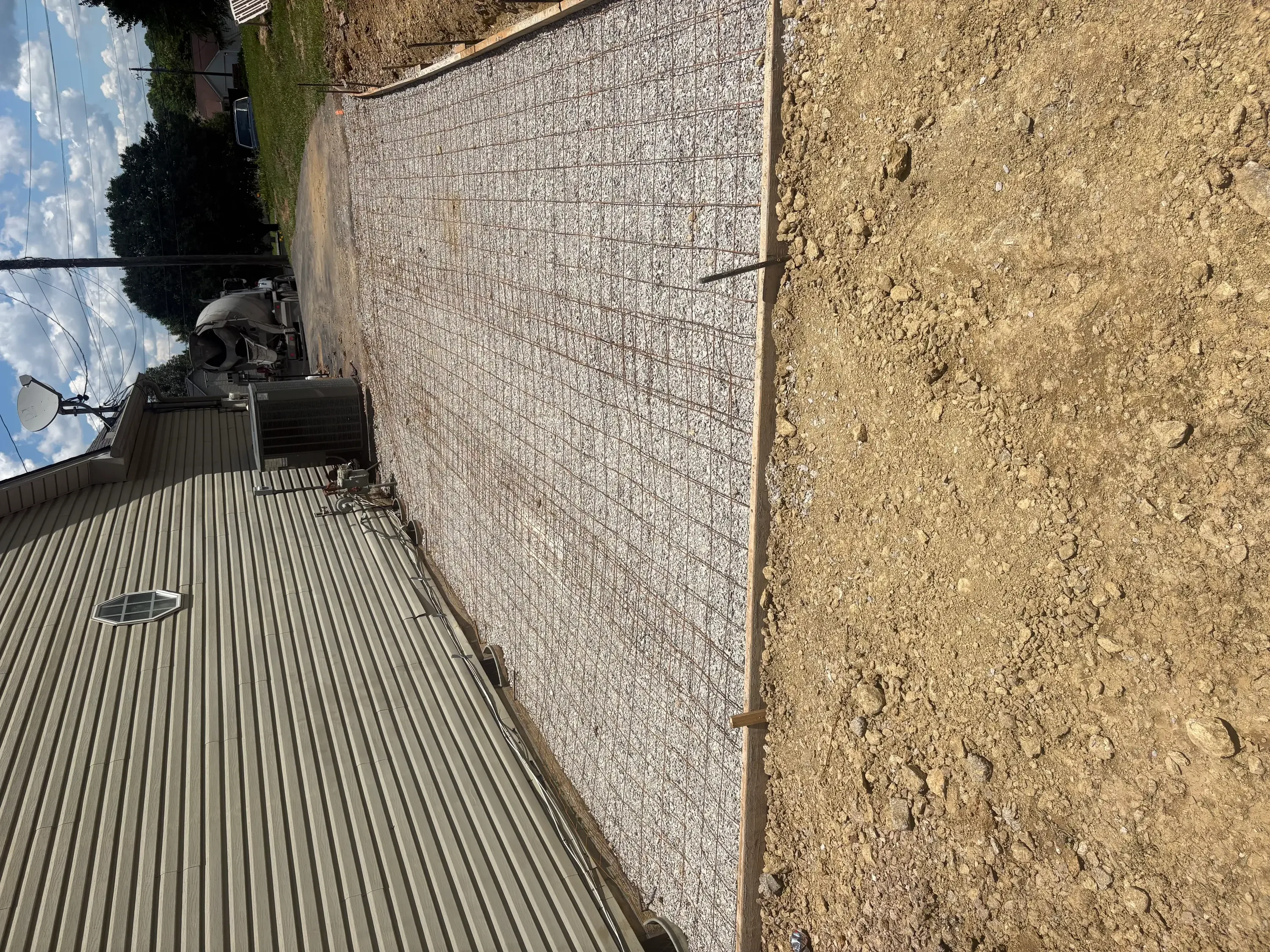 Newly installed concrete driveway with gray finish and reinforced mesh visible on adjacent prepared ground