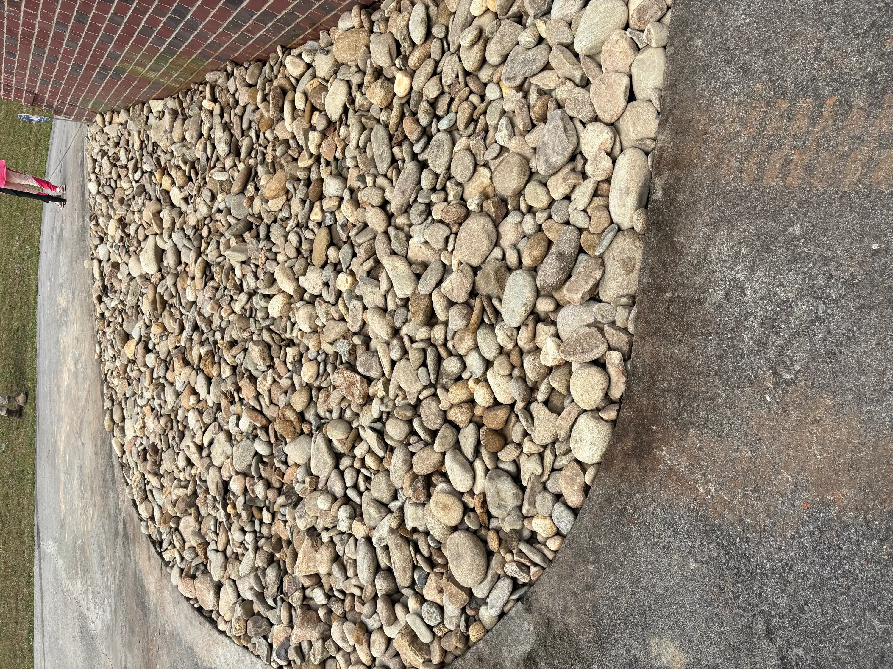 Tan river rocks installed in landscape bed next to concrete driveway