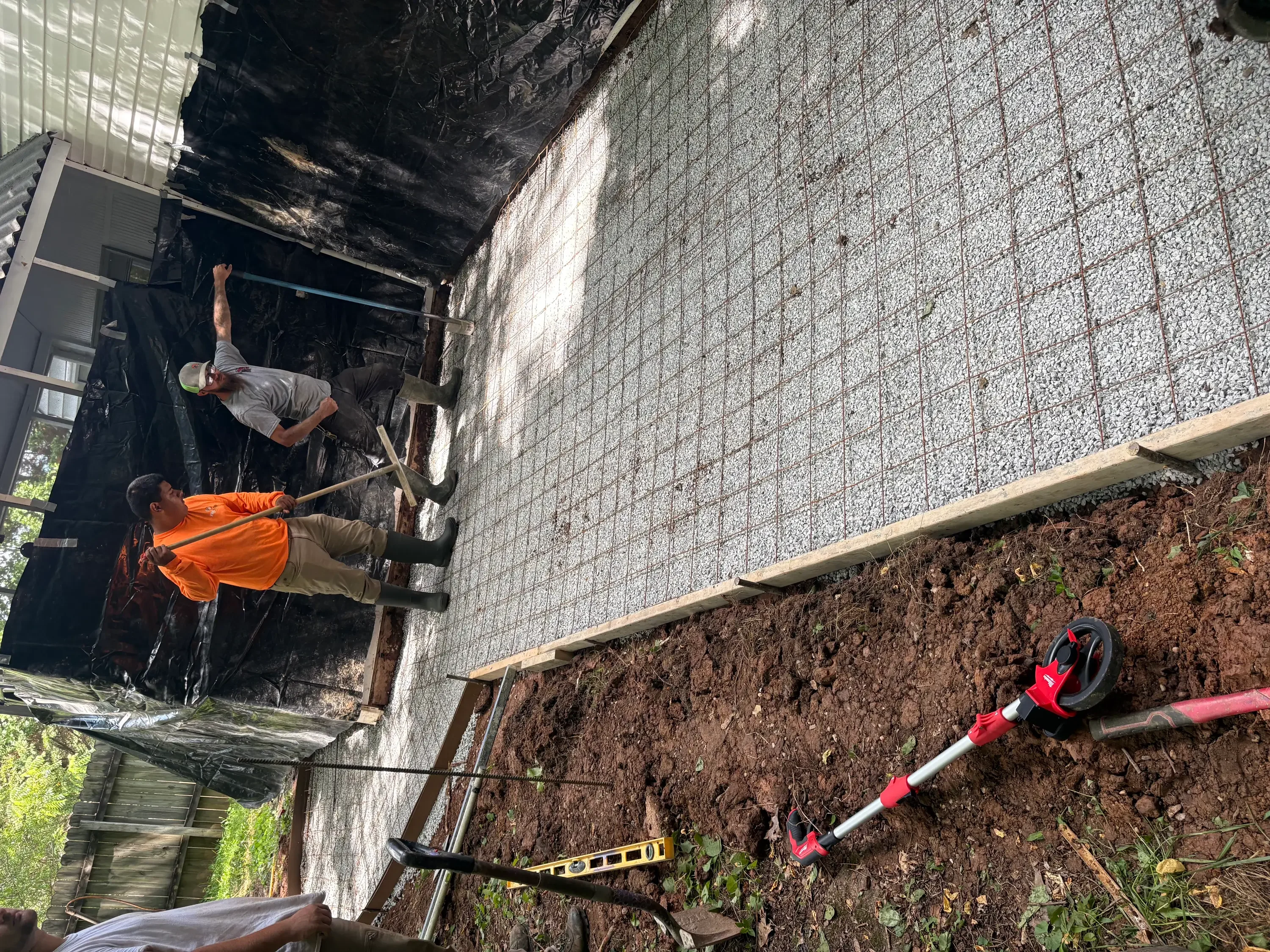 Concrete foundation wall installation with workers and equipment on prepared grade