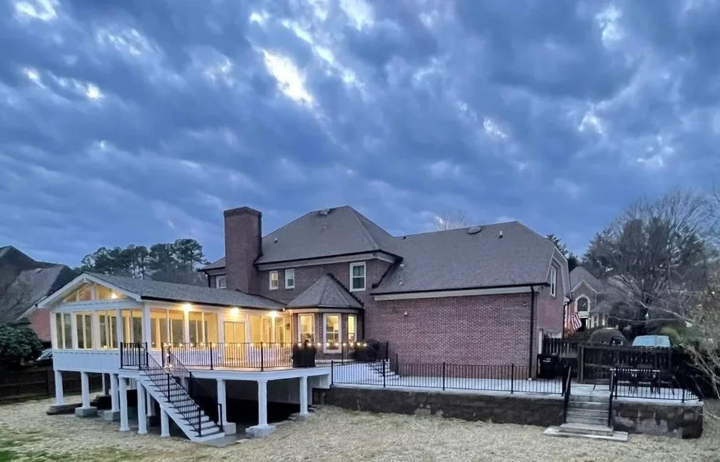 Elevated deck with concrete foundation attached to brick home at dusk