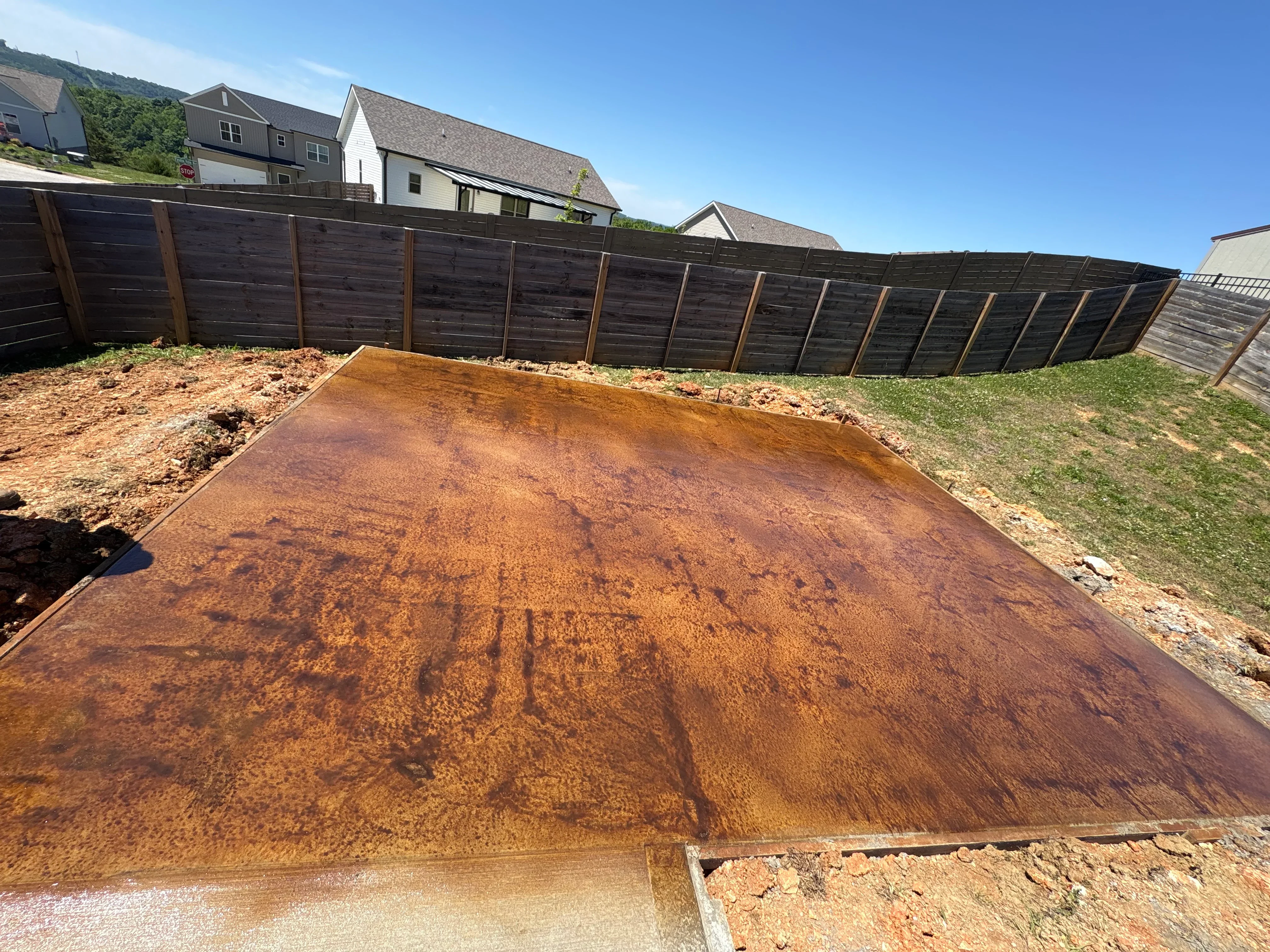 Finished concrete pad in residential backyard with wood fence and homes visible in background