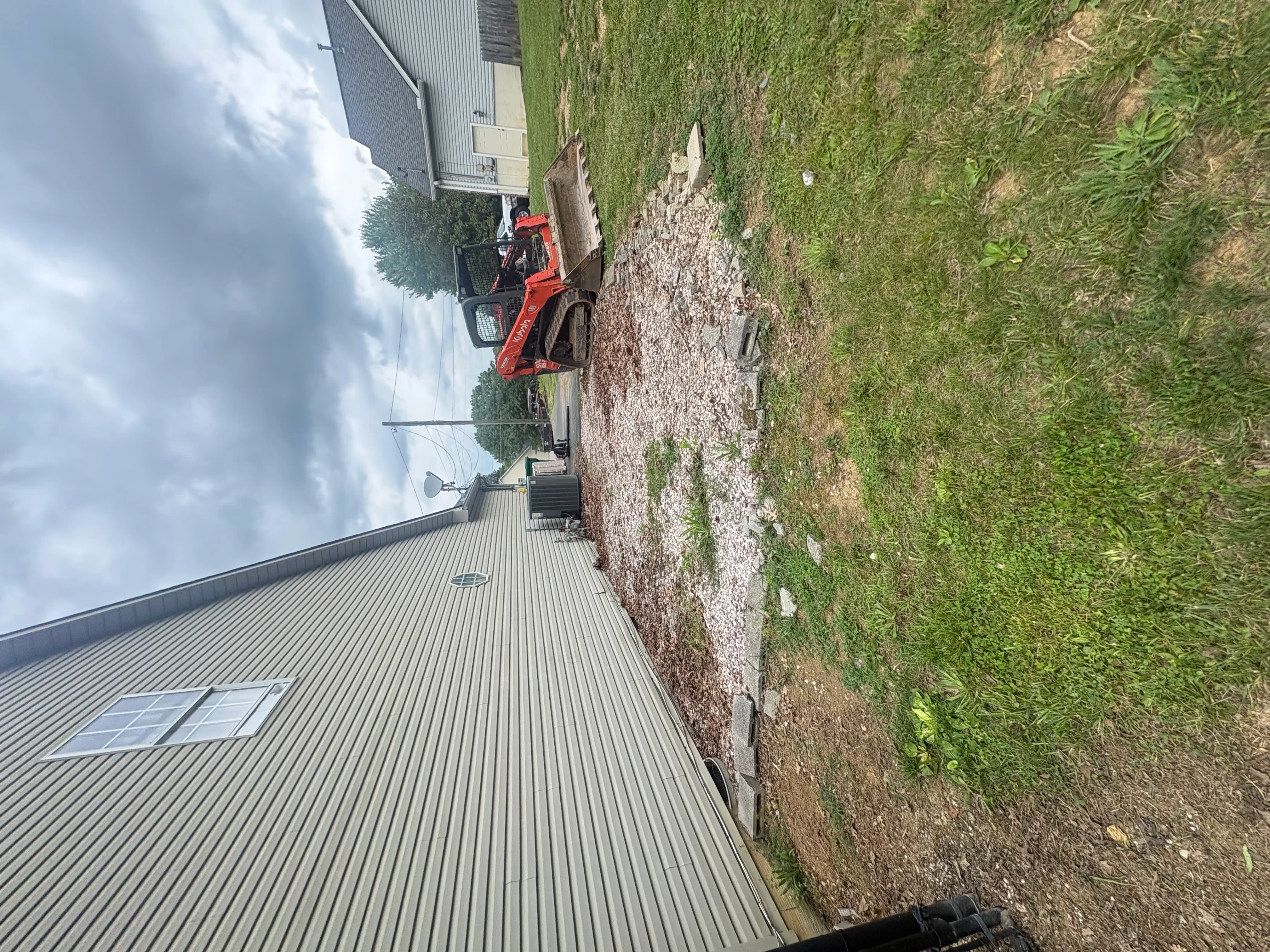 Red skid steer loader grading landscape next to finished concrete driveway