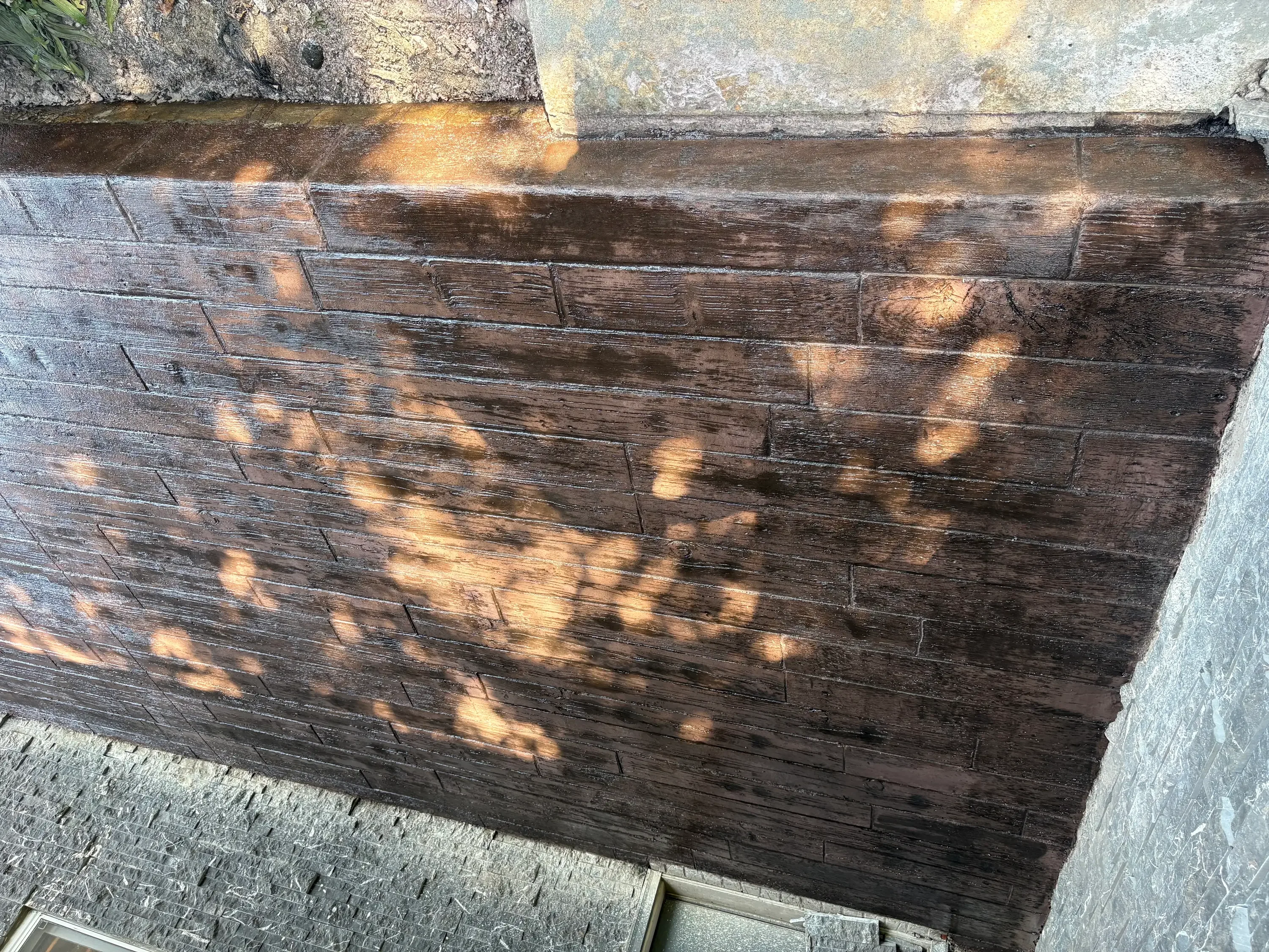 Dark stained concrete surface with wood-grain texture and sealed finish in sunlight
