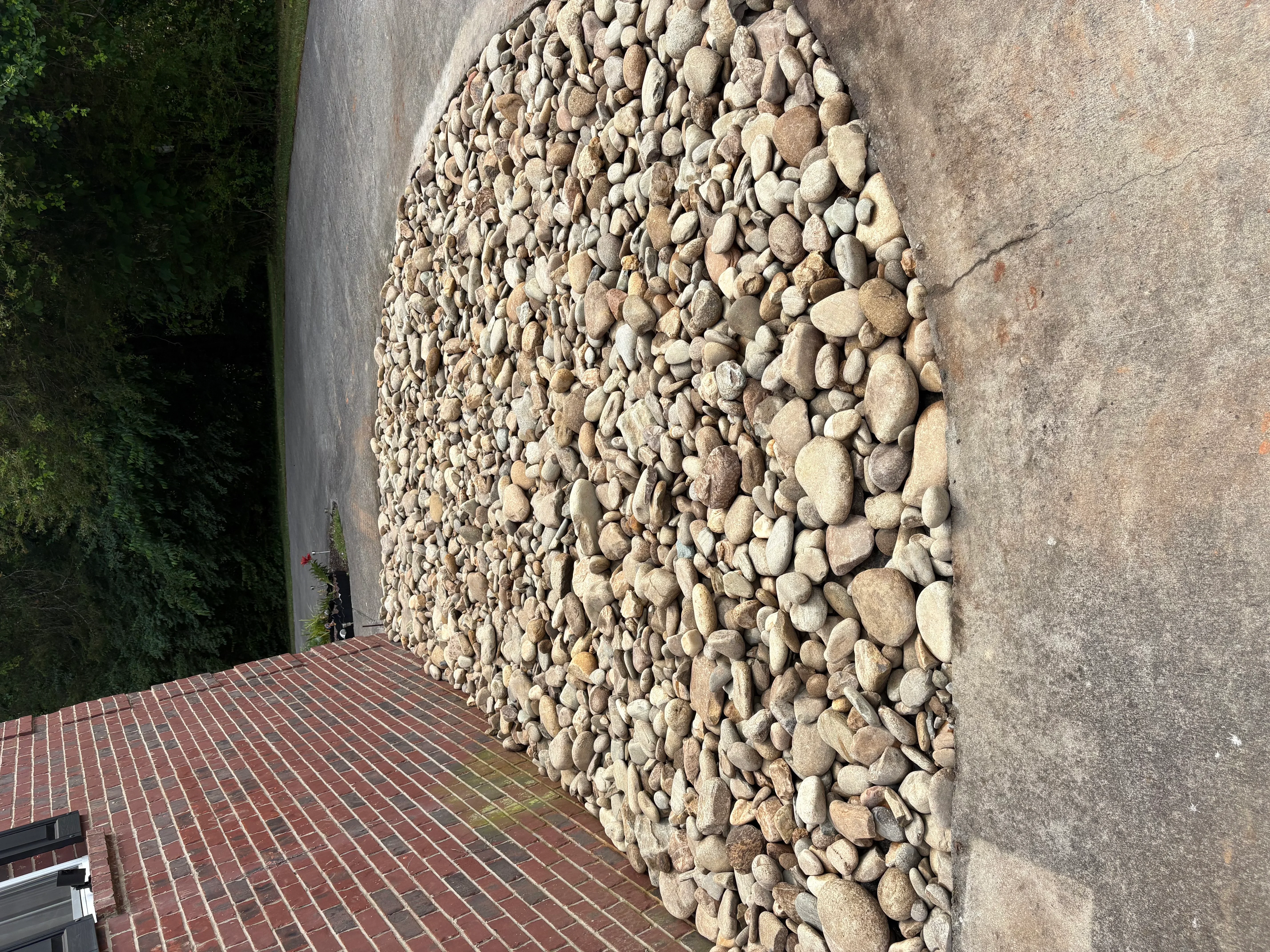 Tan and gray river rocks installed as decorative ground cover next to concrete foundation and brick patio
